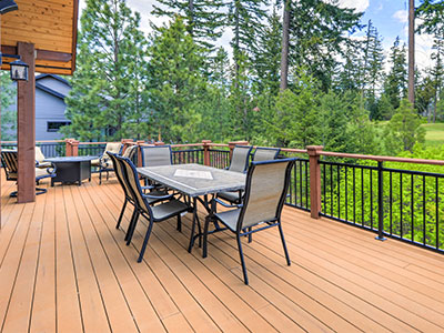 brown composite deck with metal railing and outdoor furniture set overlooking dense vegetation and tall trees