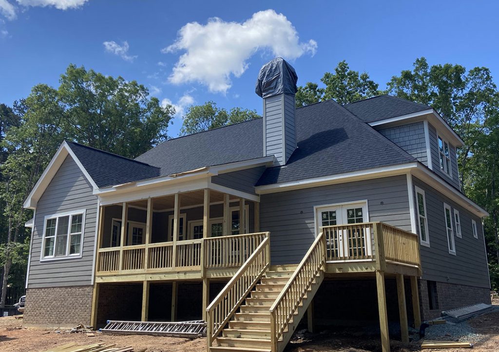 elevated wooden deck with wooden railings, partially covered, gray siding on house, dark gray shingles on roof