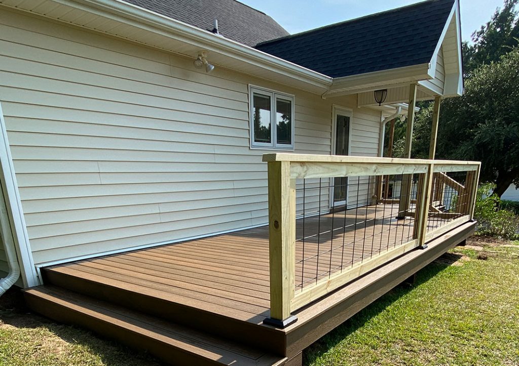 stairs leading to wooden deck with wooden railings, white siding on house, white framed windows and door, side view