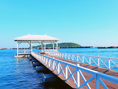 large brown pier with light colored railings leading to a covered dock and a blue sky and water background