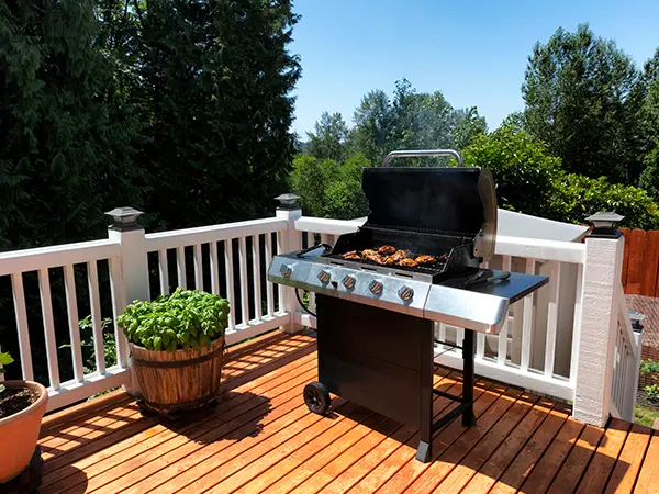 Barbeque on wooden deck with white railing.