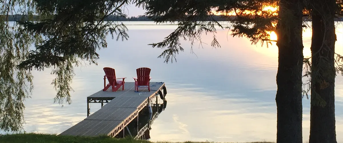 Serene dock at sunset with calm waters and red chairs.
