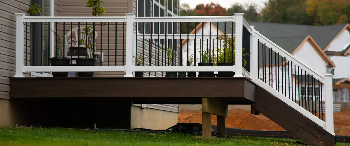 Deck Restoration in Coats Elevated deck with white and black railing, potted plants, and stairs leading to a grassy yard, near newly constructed homes.