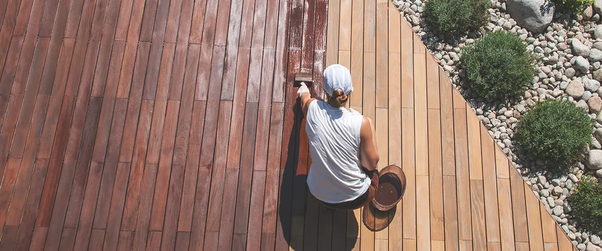 Wood deck renovation treatment, the person applying protective wood stain with a brush, overhead view of ipe hardwood decking restoration process