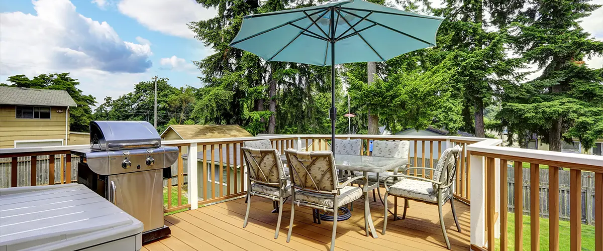 Sunny backyard deck with patio furniture, umbrella, and grill, ideal for outdoor dining, relaxation, and summer barbecues.