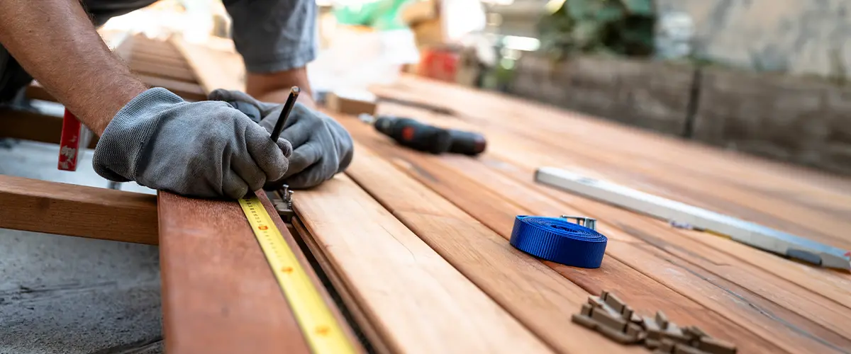 Worker with protective gloves marking a spot on wooden plank while placing it on a foundation for a deck remodeling project in Coats NC