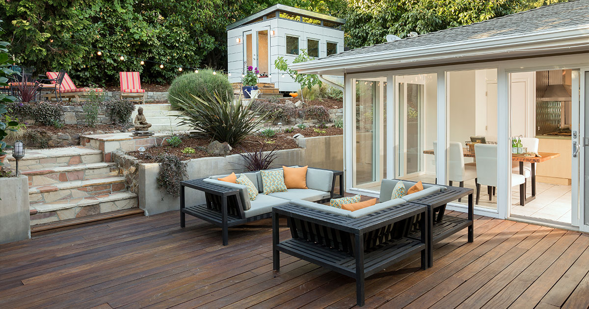 A cozy backyard patio with dark wood decking, comfortable outdoor seating, and a view of a lush, terraced garden leading to a modern garden shed.