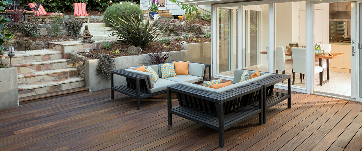 A cozy backyard patio with dark wood decking, comfortable outdoor seating, and a view of a lush, terraced garden leading to a modern garden shed.