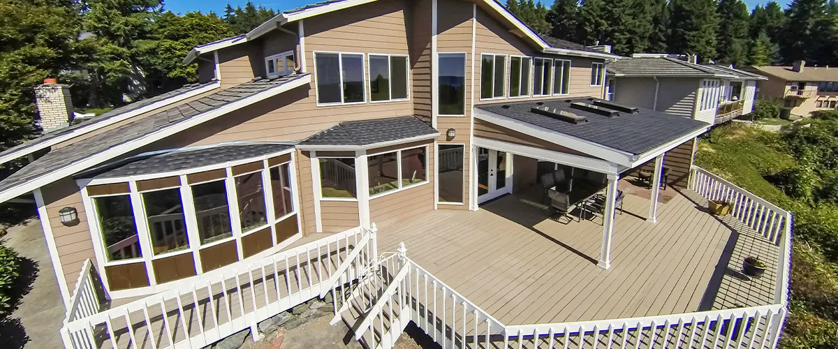 Aerial view of a spacious home with a large wooden deck and wraparound railing. Elevated deck design, residential exterior.