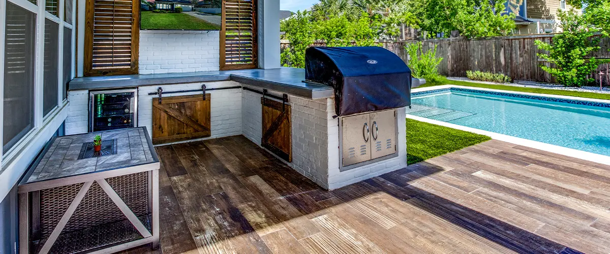 Bright open-concept outdoor kitchen on deck and dining area with large windows and seamless transition to outdoor patio with lush greenery - modern indoor-outdoor living space.