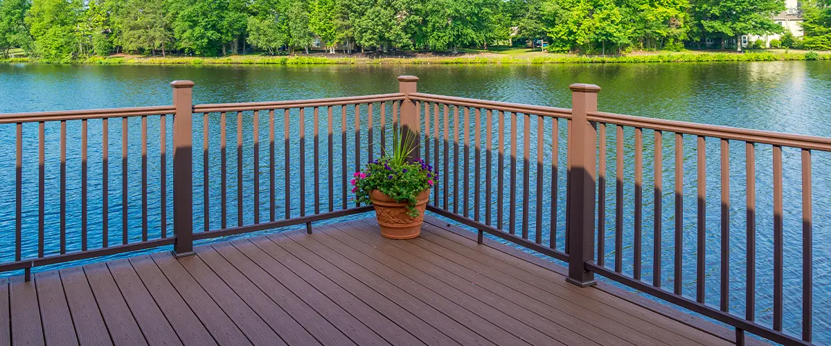 Composite deck with brown railing overlooking a serene lake, featuring a potted plant for a cozy outdoor space.