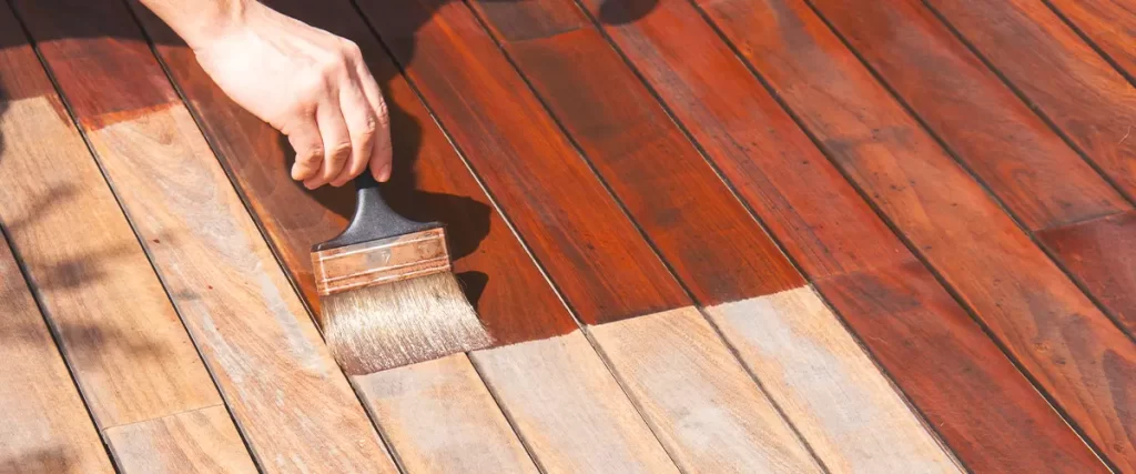 Hand applying wood stain to a deck using a paintbrush