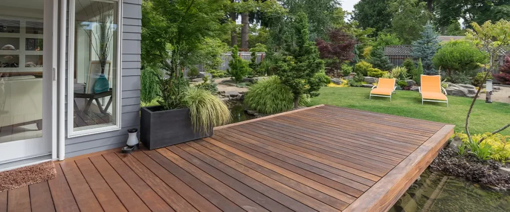 Luxury backyard deck overlooking a landscaped garden with lounge chairs and greenery.