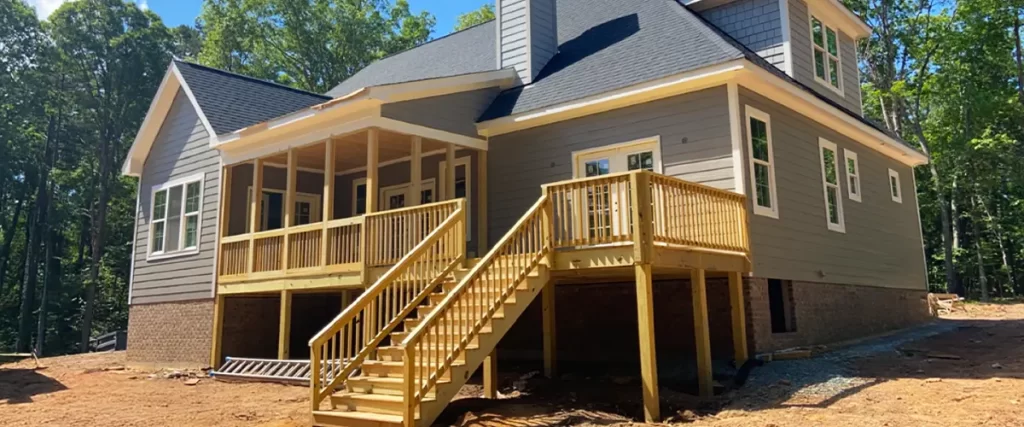 Back view of new home construction with covered porch, pressure-treated wood deck, and staircase in wooded area