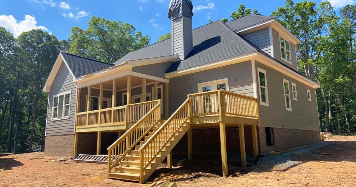 Back view of new home construction with covered porch, pressure-treated wood deck, and staircase in wooded area