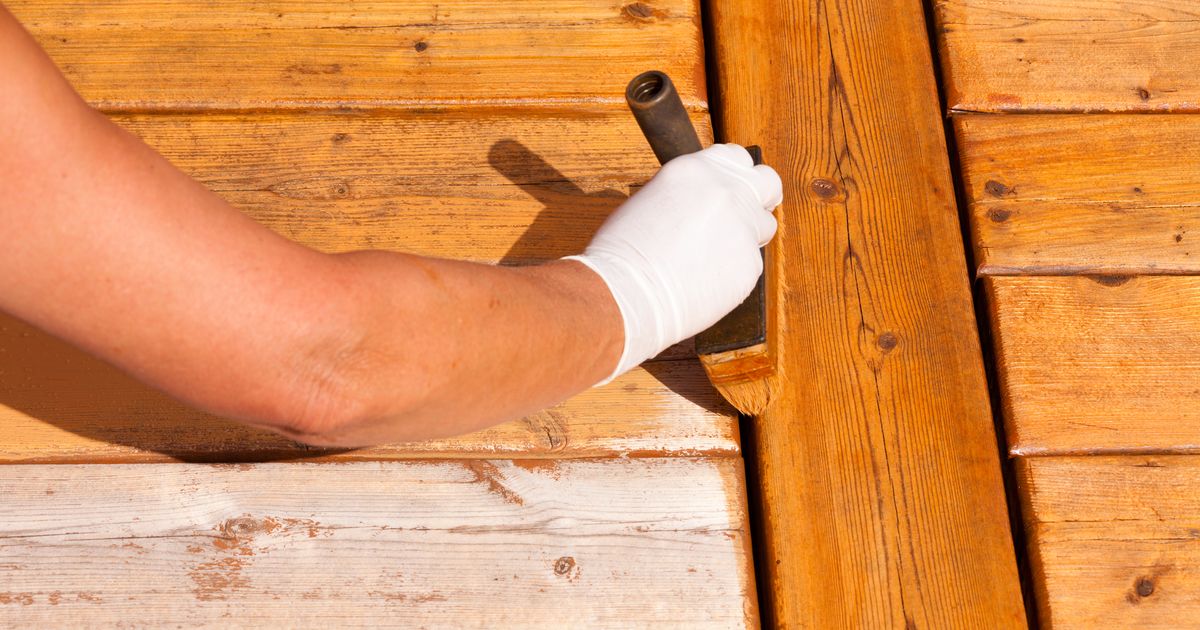 A professional hand using a brush to apply a golden finish to wood, helping homeowners decide between a transparent semi transparent deck stain for their outdoor project.