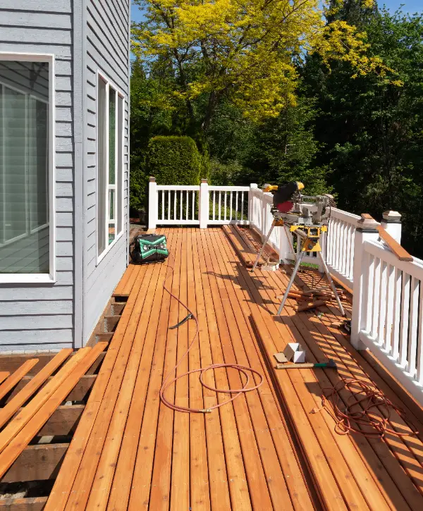 a wooden deck being repaired, with new wooden planks being installed on a house's exterior