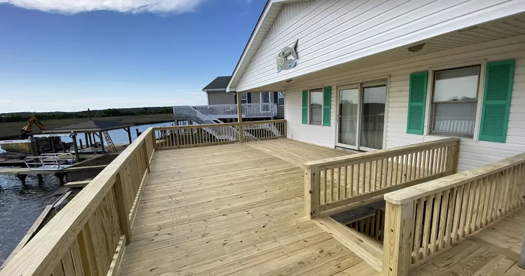 Large waterfront wood deck with railings and outdoor living space attached to lakeside home
